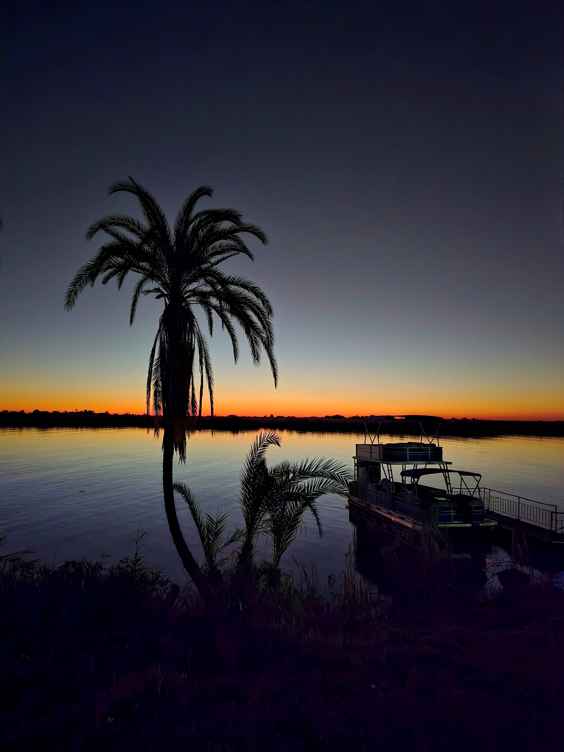 This image is of the setting sun with the palm trees and boat on the Chobe river